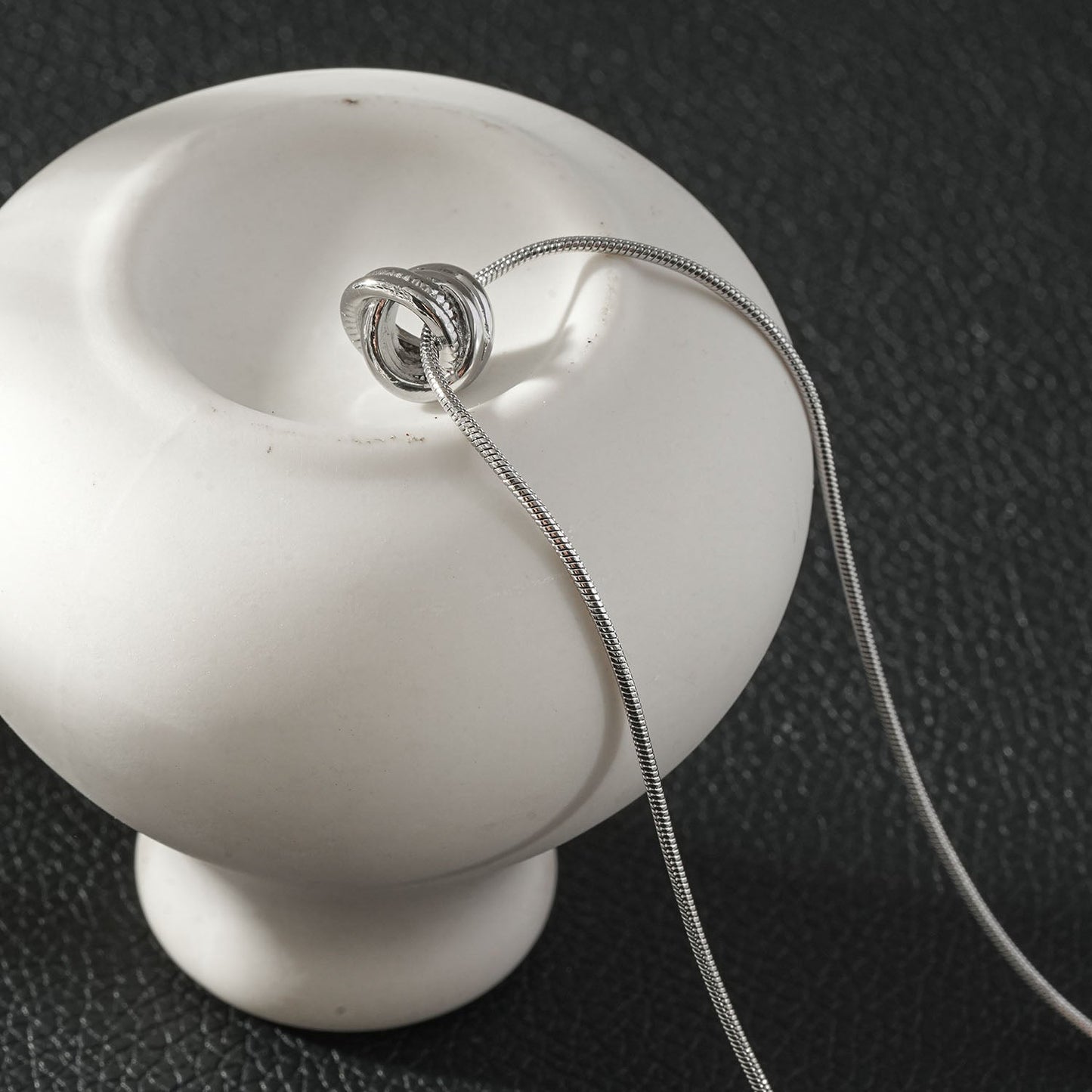 HACKNEY NINE Jewelry ALEKI Silver white gold sculptural knot pendant necklace, close-up shot showing intricate design and polished finish.