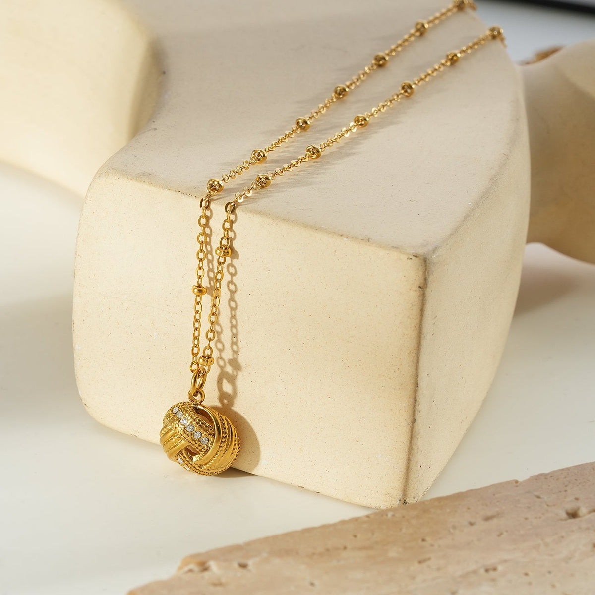 HACKNEY NINE Jewellery SALAMASINA Gold crystal interwoven knot pendant necklace, close-up of intricate gold jewelry design.
